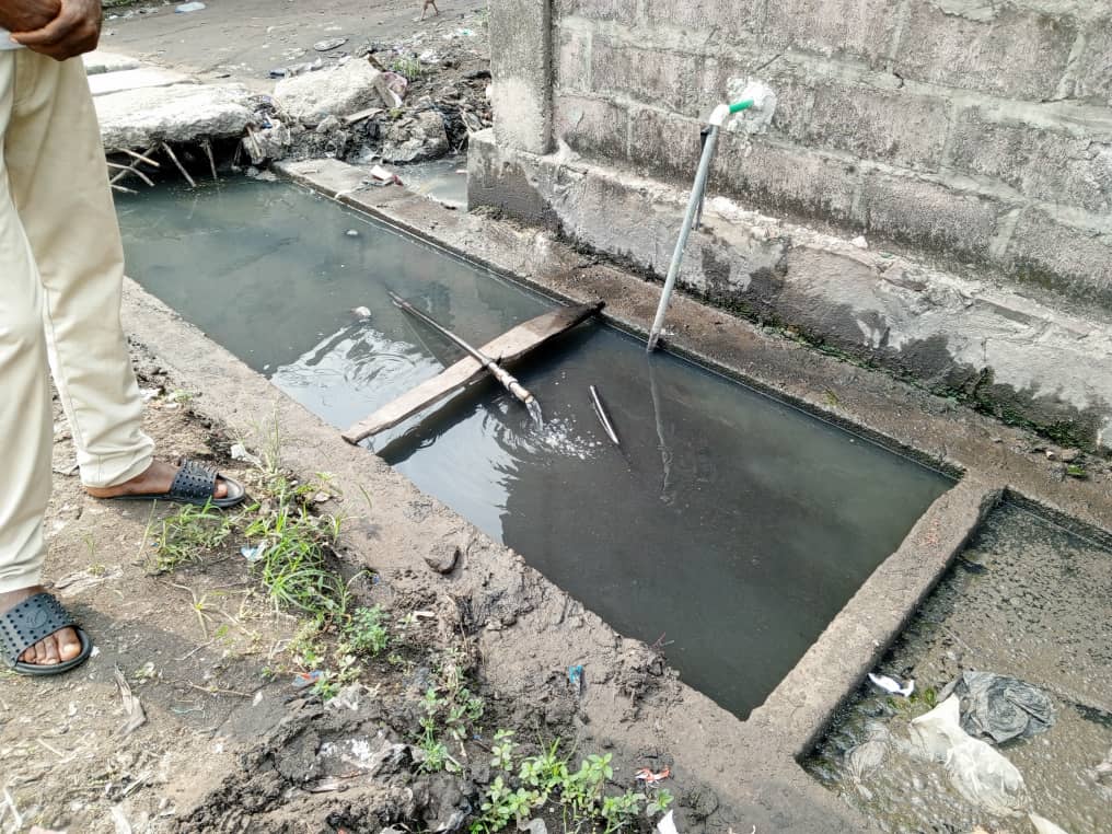 Un tuyau de distribution d'eau de la Regideso en PVC coupé et baignant dans un caniveau rempli d'eau usée. Photo Lemag.cd.